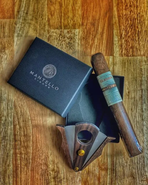 A Mantello leather cigar case and cutter beside a cigar on a wood table